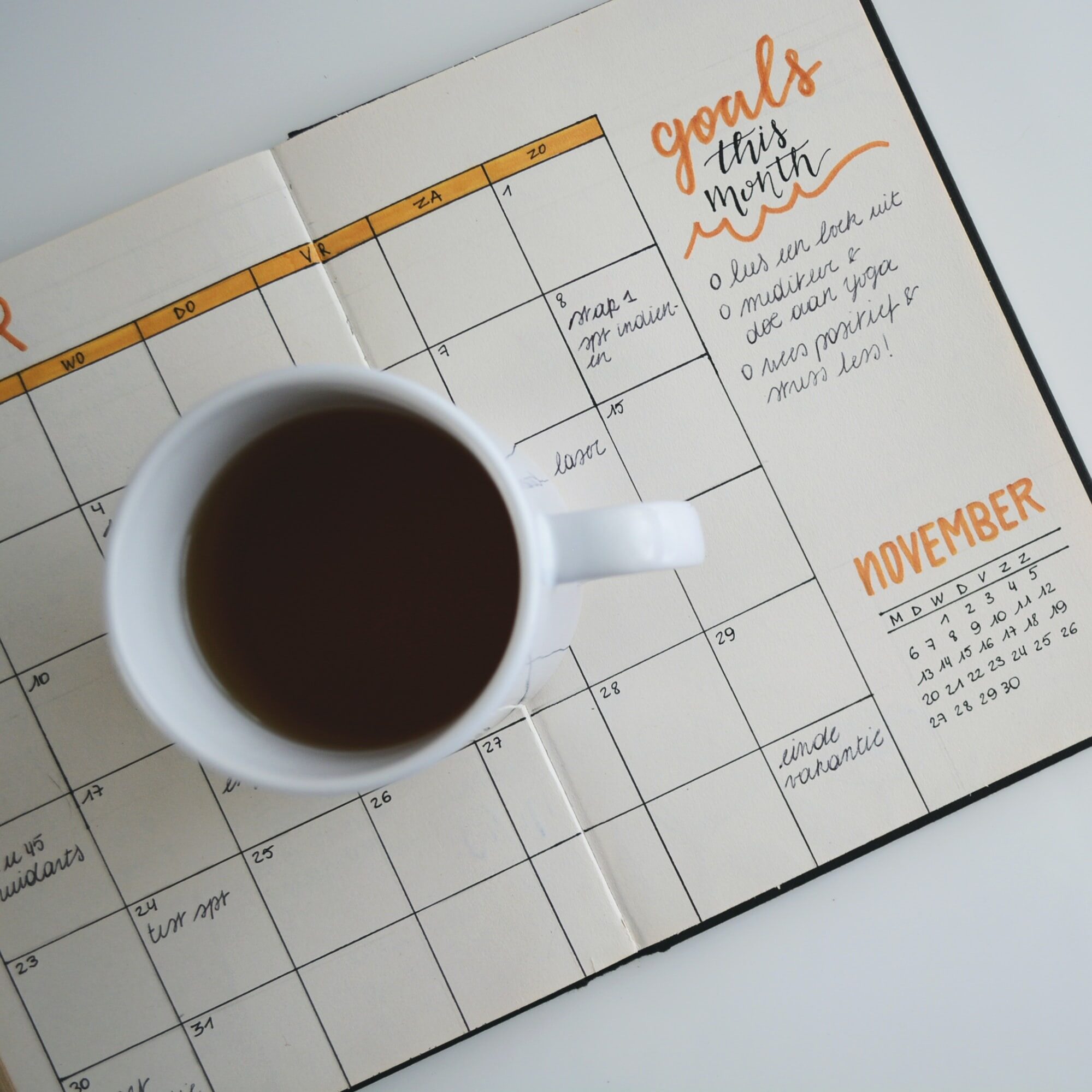 white ceramic mug with coffee on top of a planner