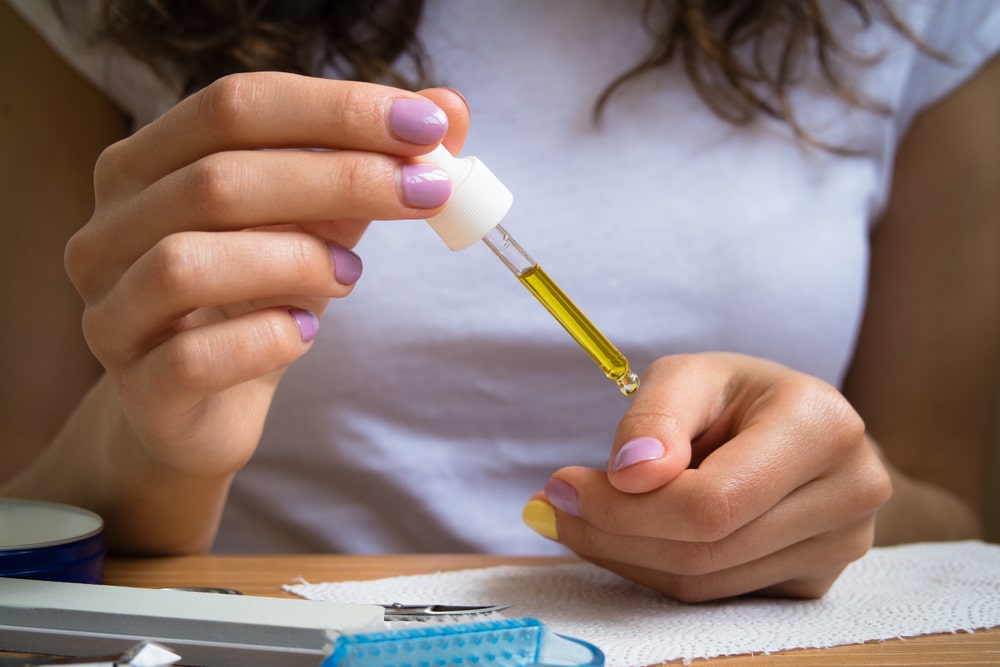 woman placing cuticle oil on her polished nails